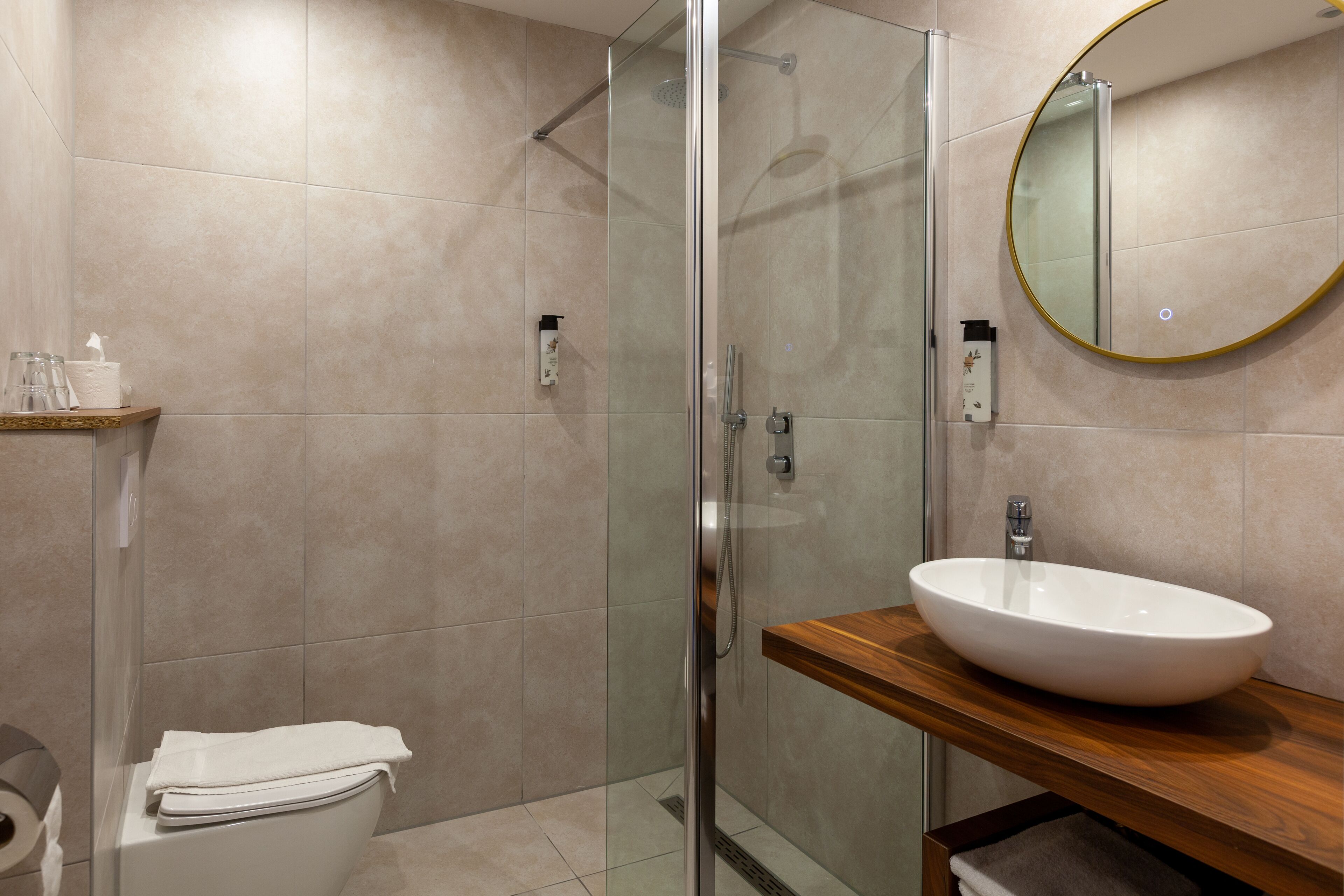 A modern bathroom with a glass-enclosed shower, a white sink on a wooden countertop, and a toilet with a towel on top.