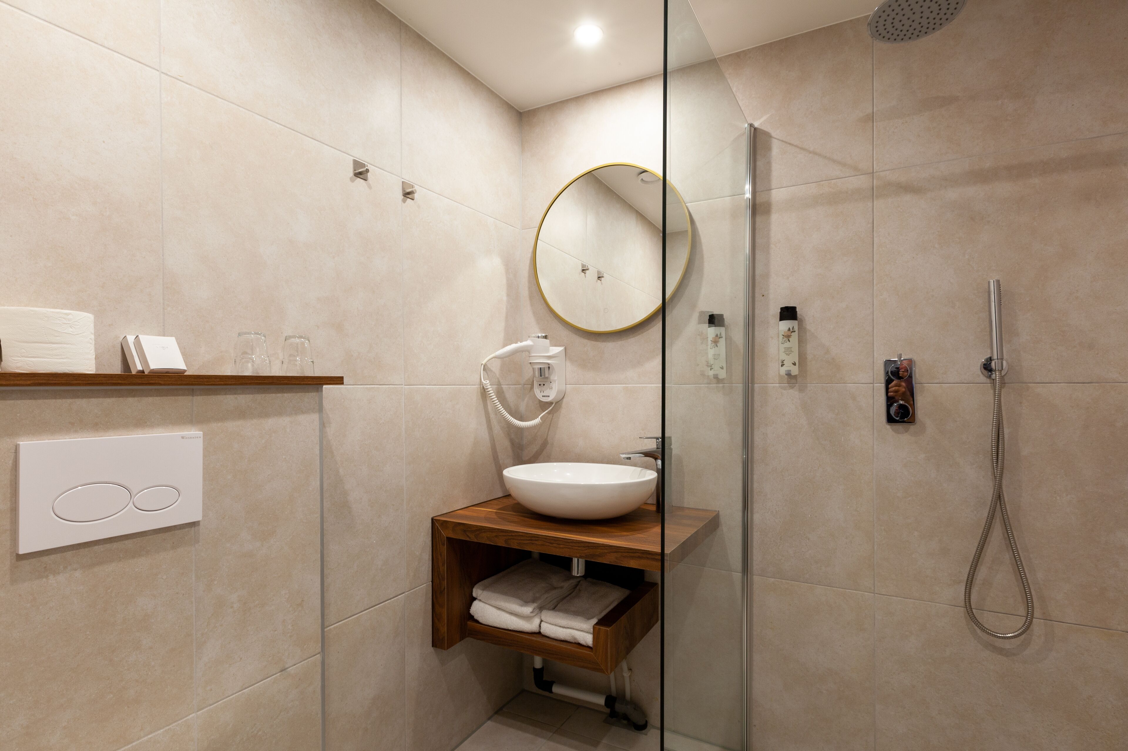 A modern bathroom with a round mirror, a white sink, and a glass-enclosed shower.