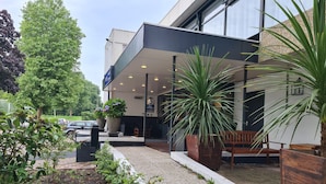 A modern building with a covered outdoor seating area, potted plants, and a gravel pathway.