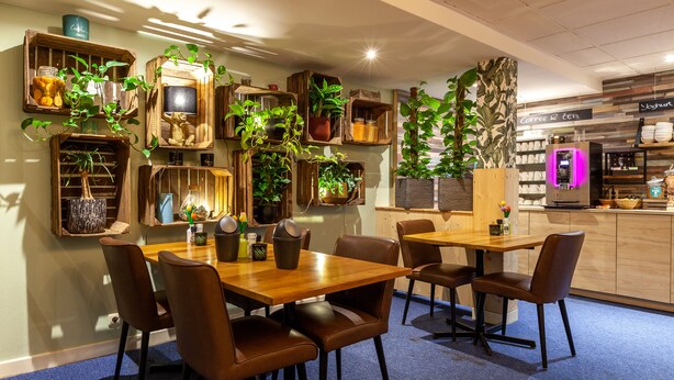 A restaurant with wooden tables and chairs, potted plants, and a coffee machine.