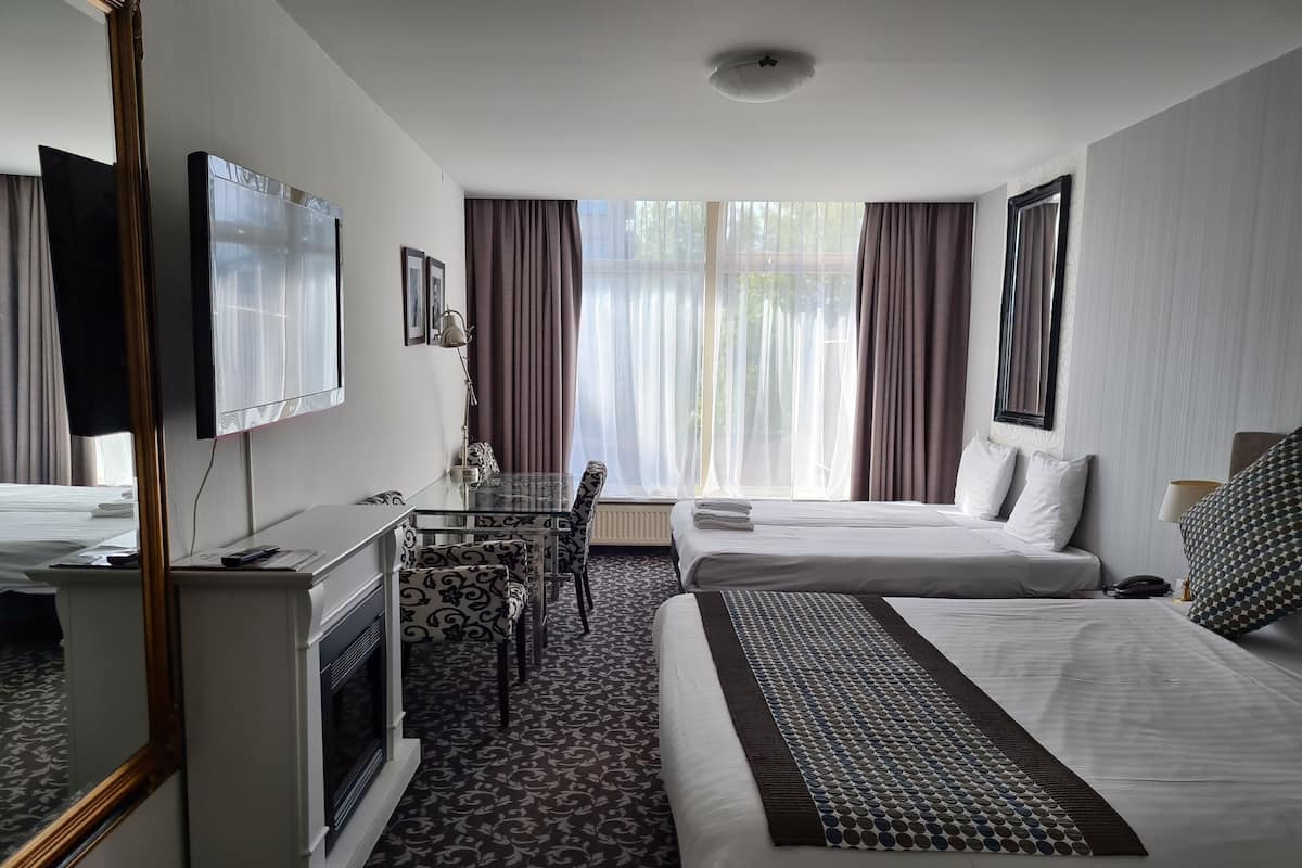 A hotel room with a glass dining table, two beds, a TV, and a large window with curtains.