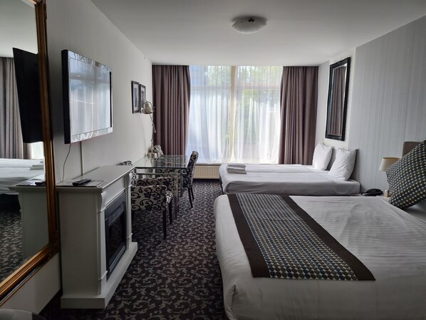 A hotel room with a glass dining table, two beds, a TV, and a large window with curtains.