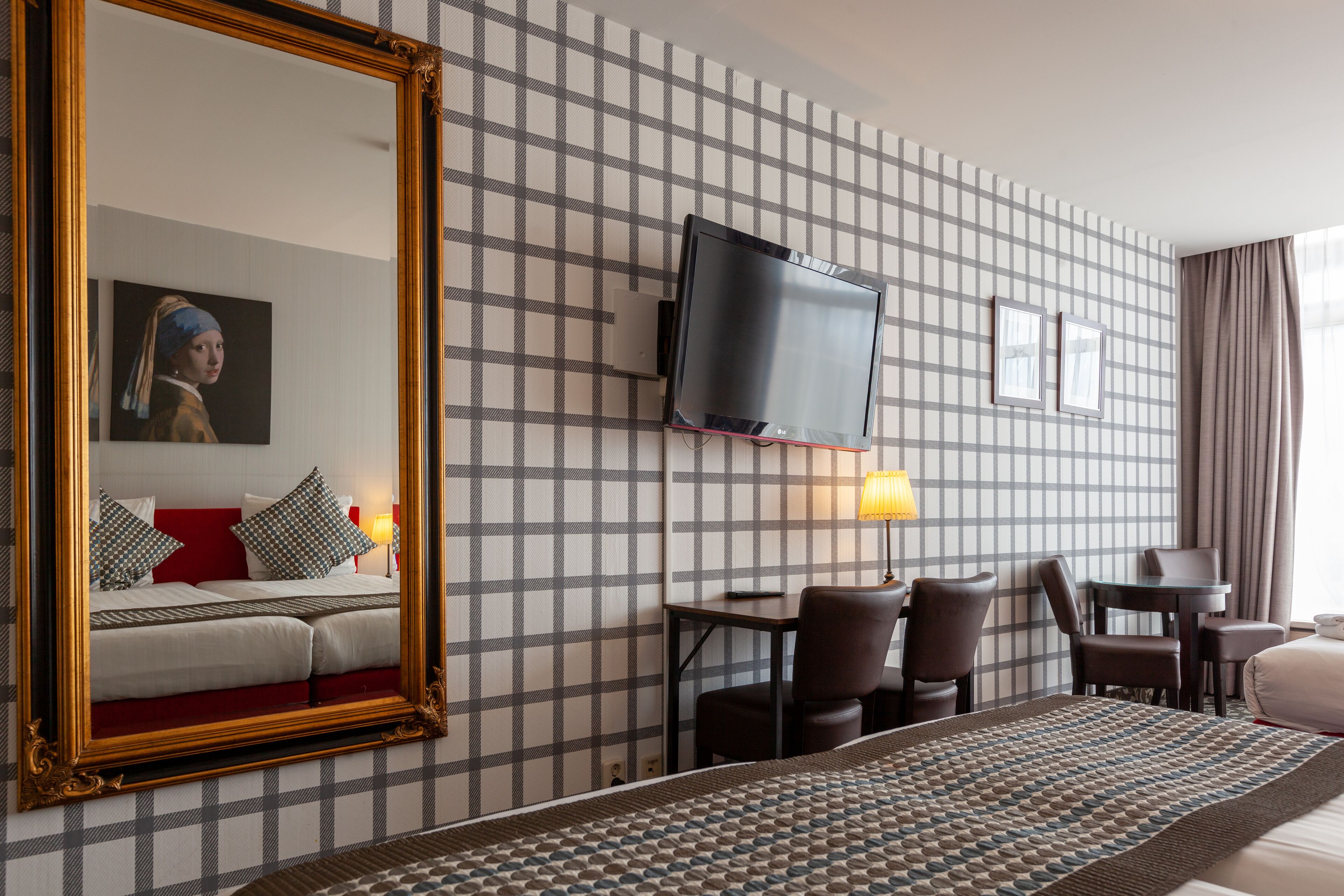 Habitación de hotel con una cama grande, un televisor montado en la pared, un escritorio con sillas y un estampado de cuadros en la pared.