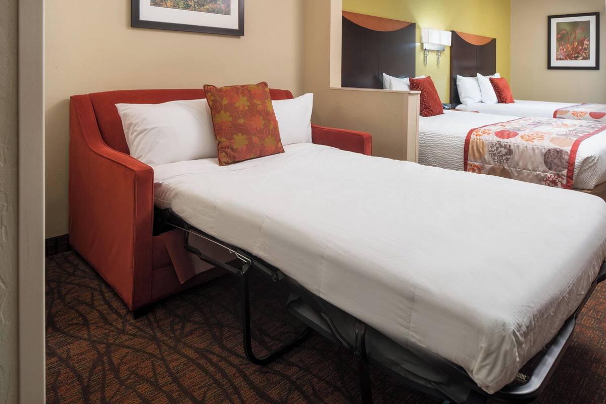 Habitación de hotel con una cama individual, un sofá y otra cama al fondo.