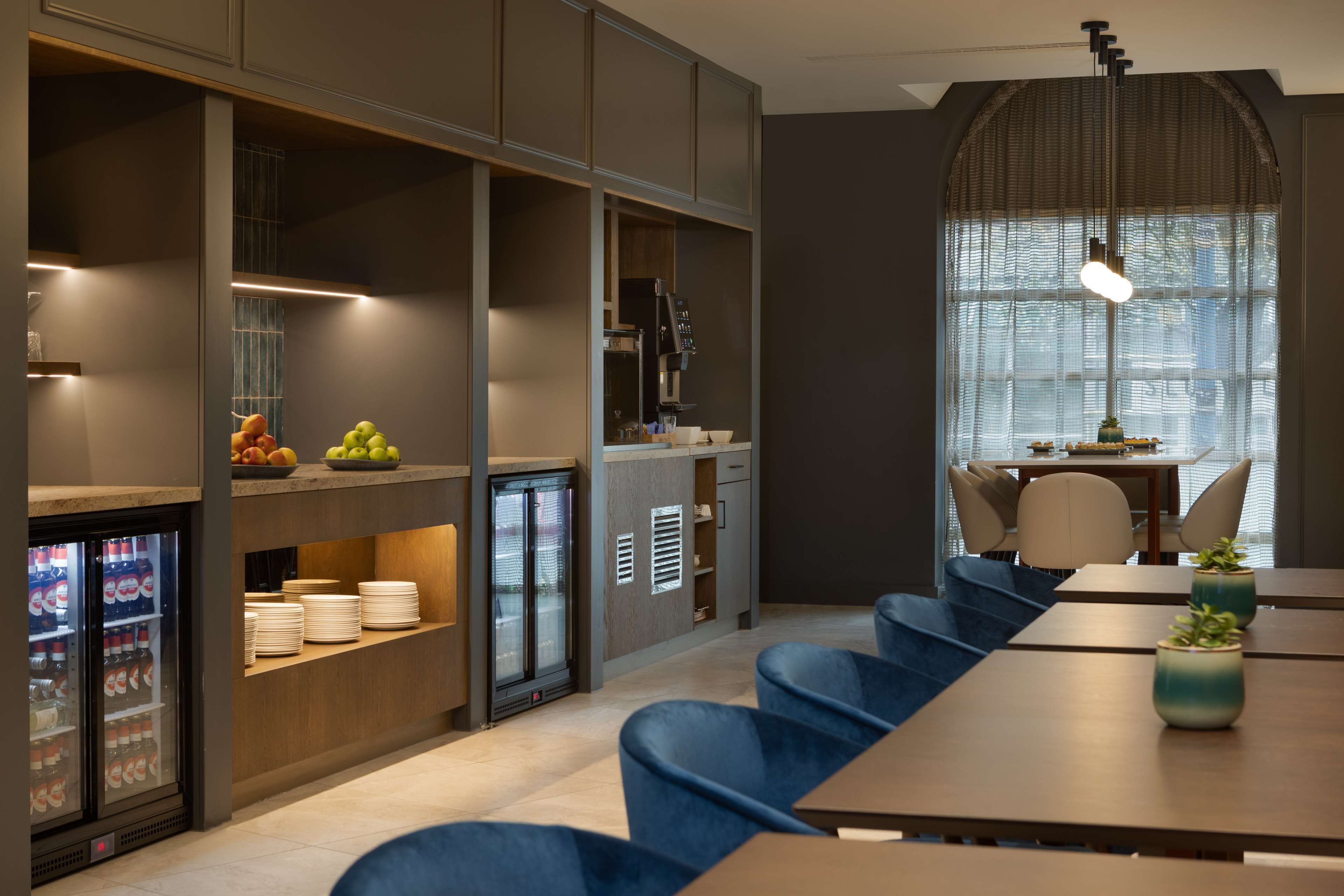 A modern kitchen with built-in appliances, a refrigerator, and a dining area with blue chairs and a wooden table.