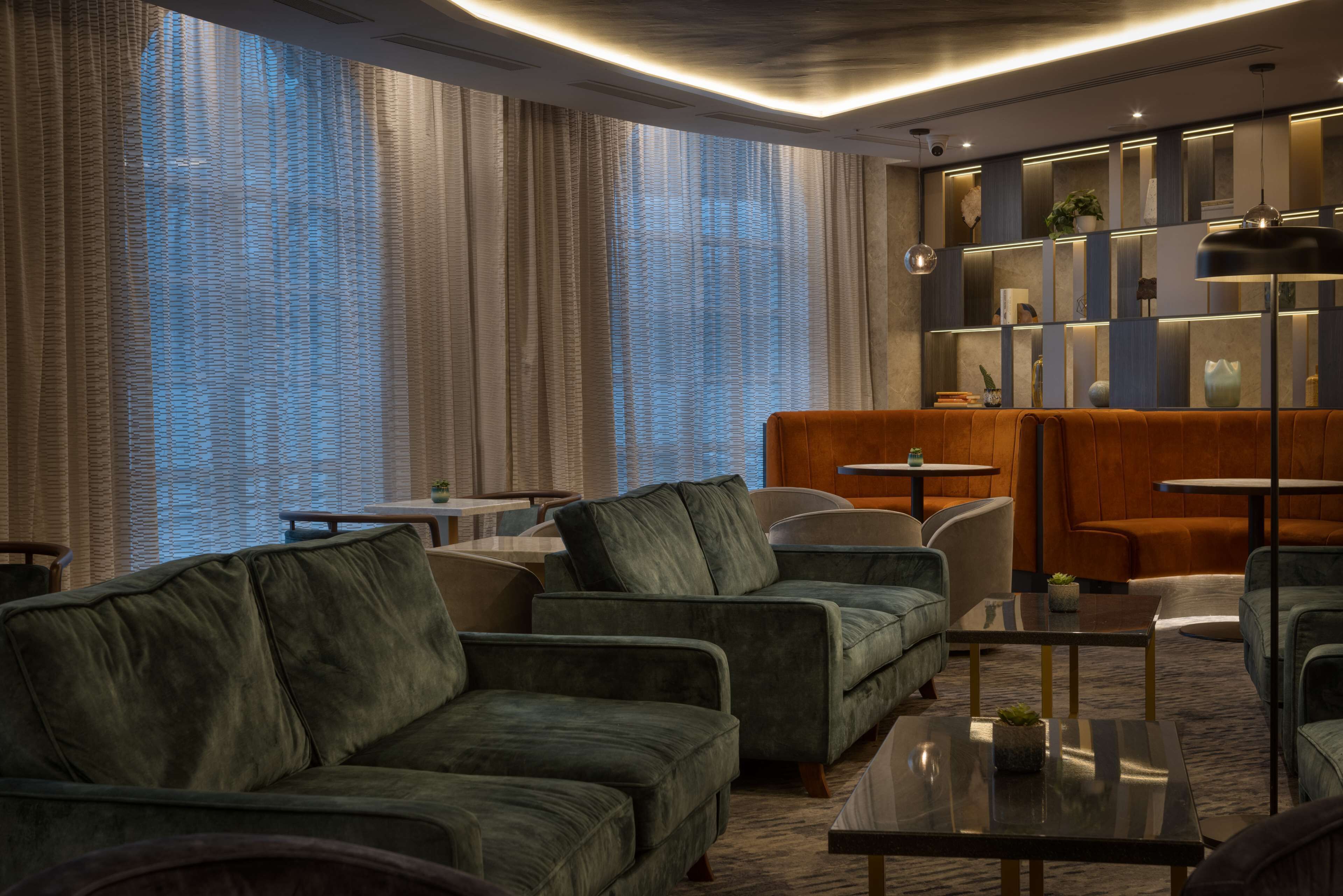 A modern hotel lobby with green sofas, a wooden reception desk, and a large window with curtains.