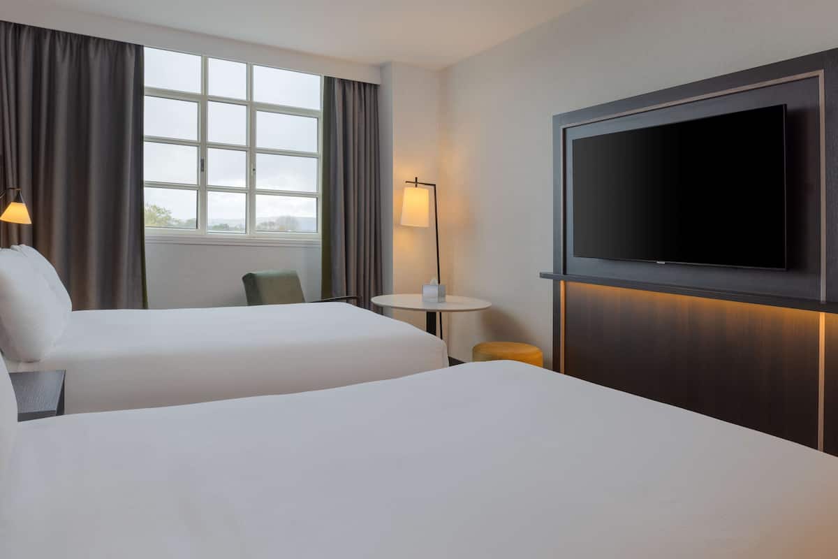 A hotel room with two beds, a TV, a small table, and a lamp.
