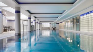 A long indoor swimming pool with clear blue water, surrounded by white walls and columns, and a tiled floor. - Hilton Cardiff (Cardiff)