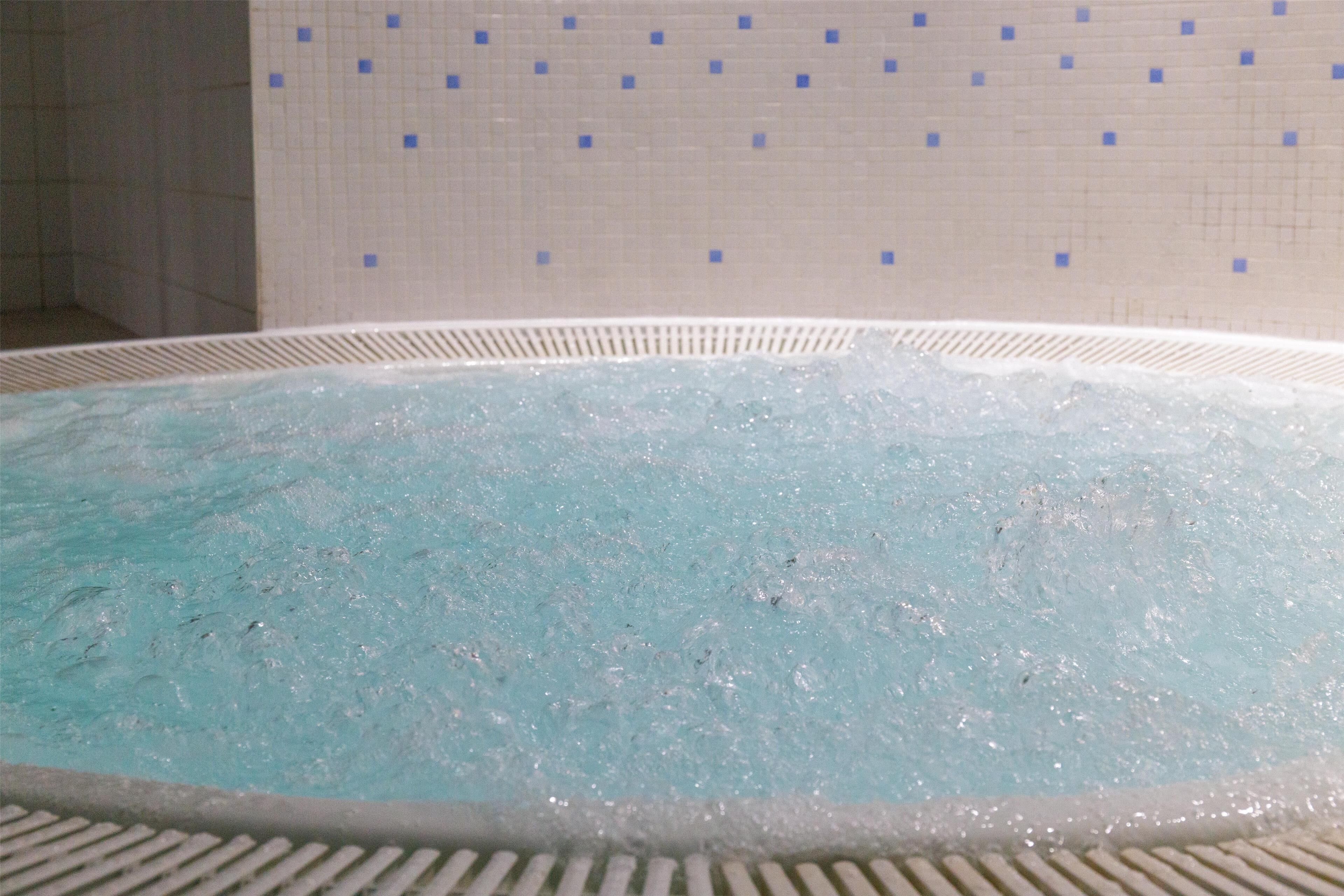 A hot tub with a tiled wall in the background.