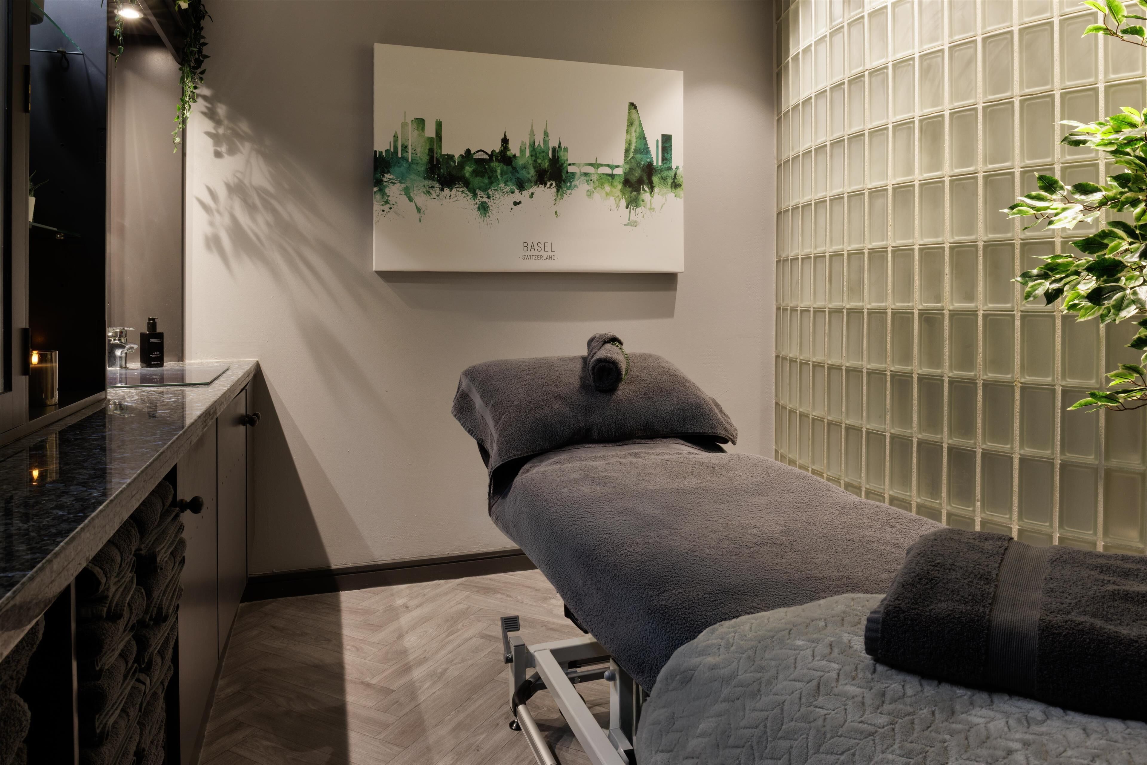 A spa room with a massage table, a cityscape artwork, and a glass partition.
