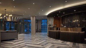 A modern hotel lobby with a herringbone patterned floor, a reception desk, and a seating area with a sofa. - Hilton Cardiff (Cardiff)