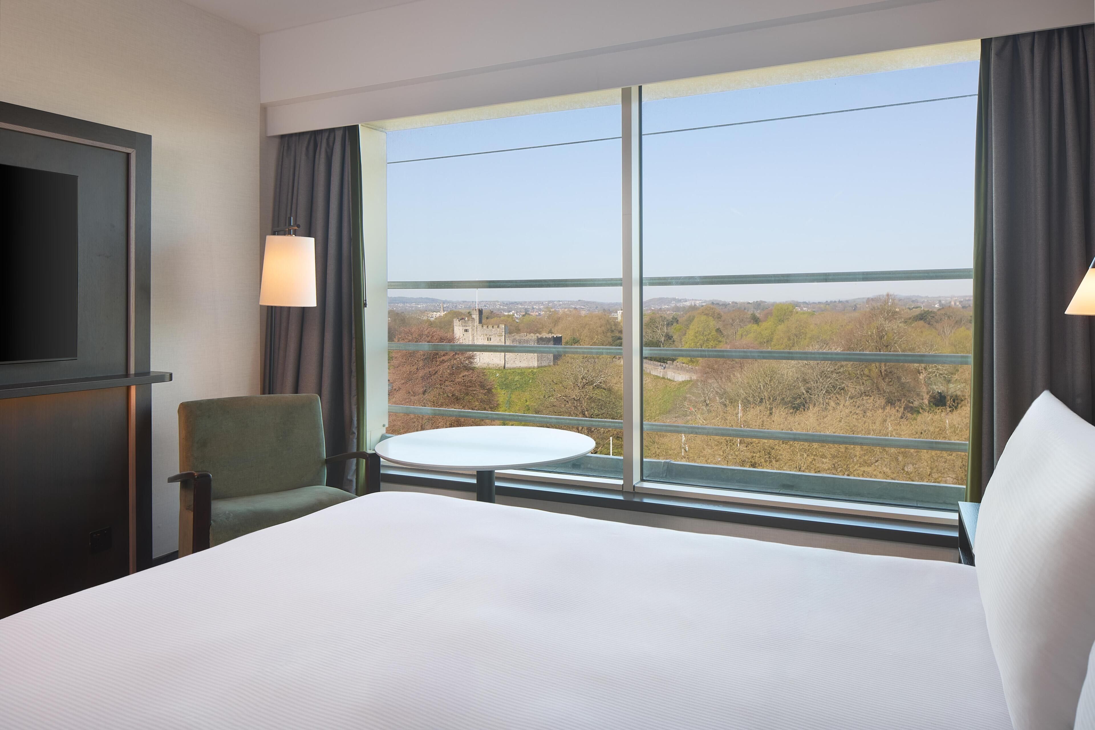 A hotel room with a large bed, a chair, a small table, and a TV.