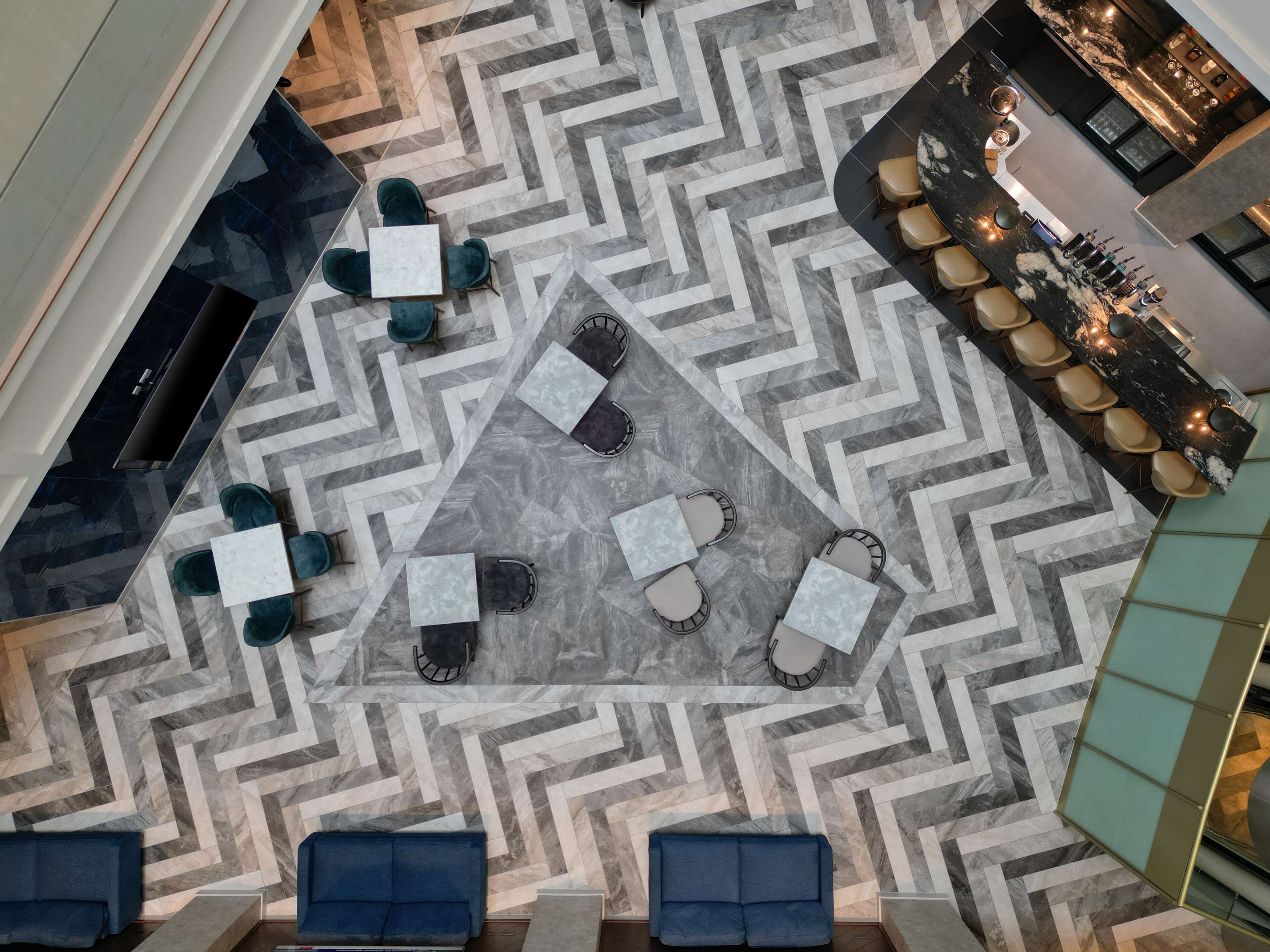 Et moderne loungeområde med et geometrisk gulvmønster, forskellige siddepladser og en bardisk.