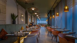 A restaurant with a long counter, multiple tables, and chairs. There are hanging lights and a plant on the wall. - Hilton Cardiff (Cardiff)