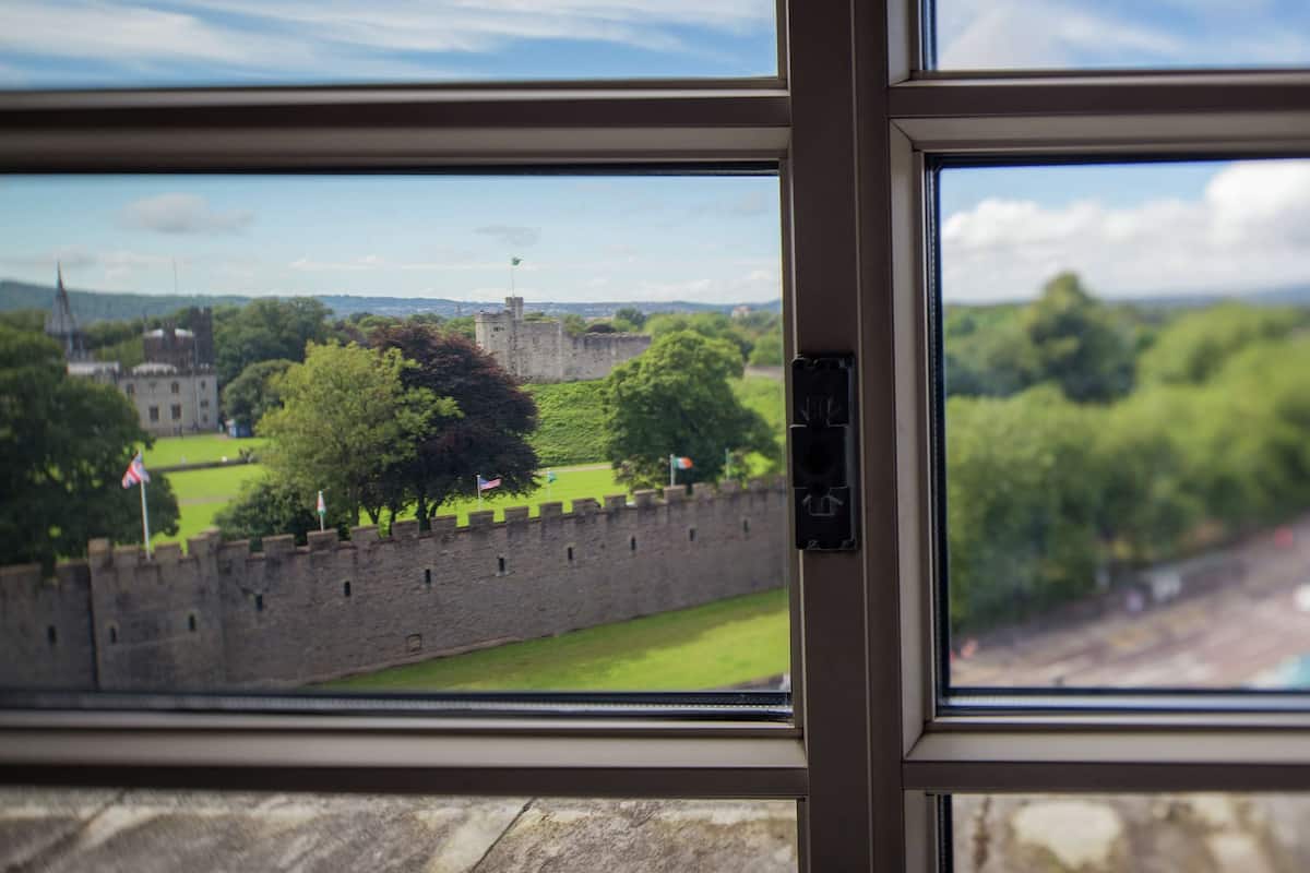 A view through a window with a stone wall and a grassy area in the foreground.