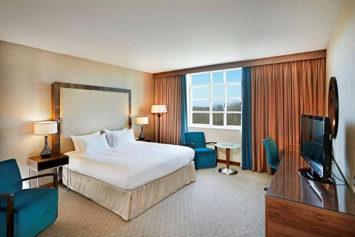 A hotel room with a large bed, two bedside tables with lamps, a TV, a desk, and a chair.