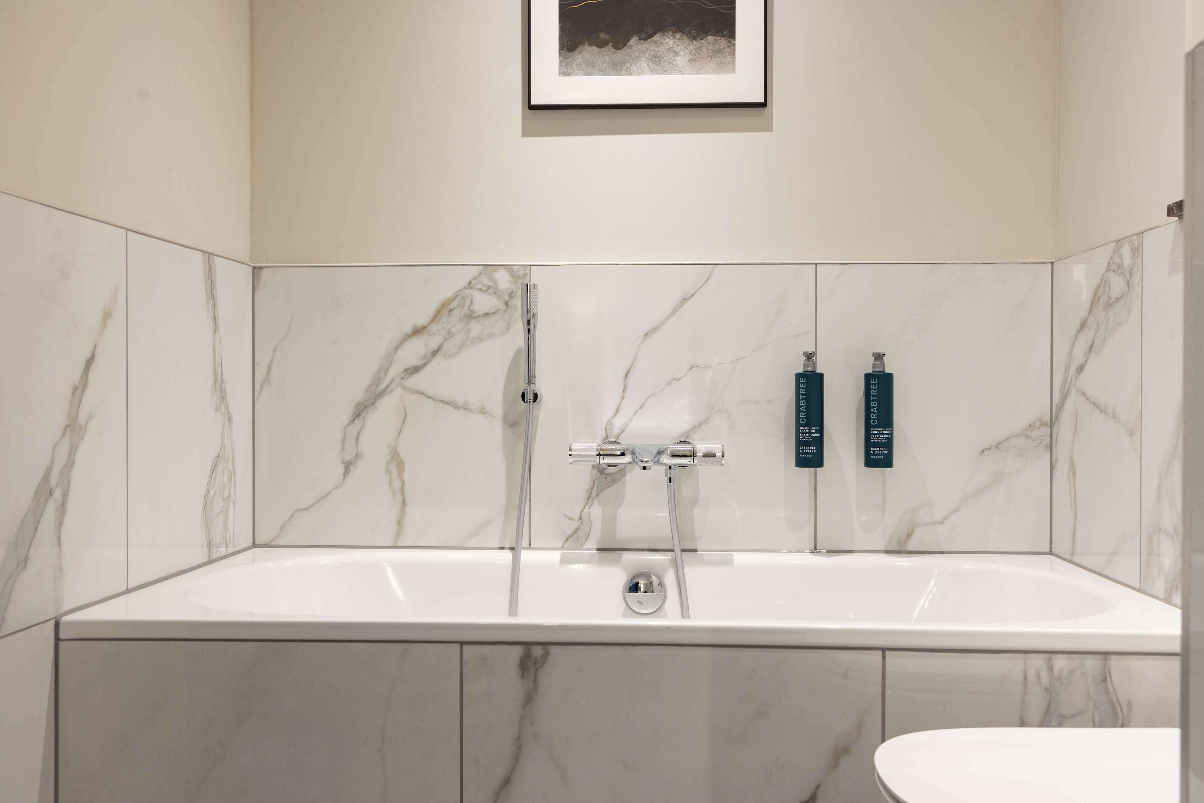 A bathroom with a marble-tiled wall, a bathtub, and two bottles of shampoo.