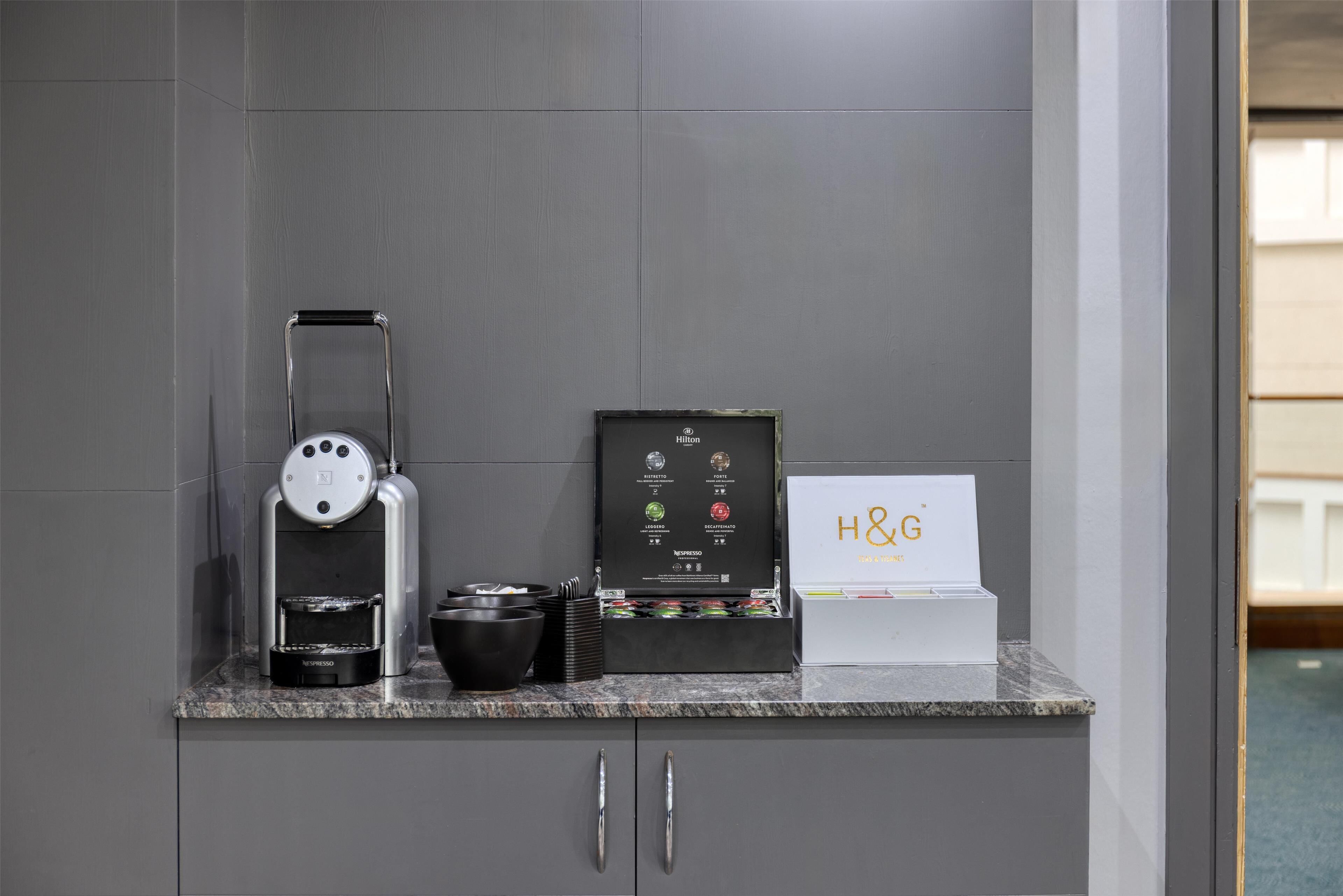 A kitchenette with a coffee maker, a Nespresso machine, and a display of coffee pods.