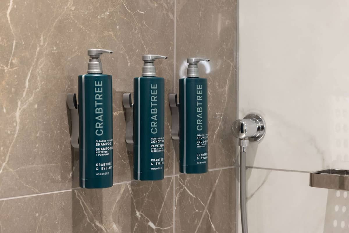 Three bottles of Crabtree & Evelyn shampoo and conditioner on a marble wall.