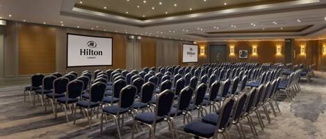 A conference room with rows of blue chairs, a large screen, and a "Hilton Cardiff" sign.