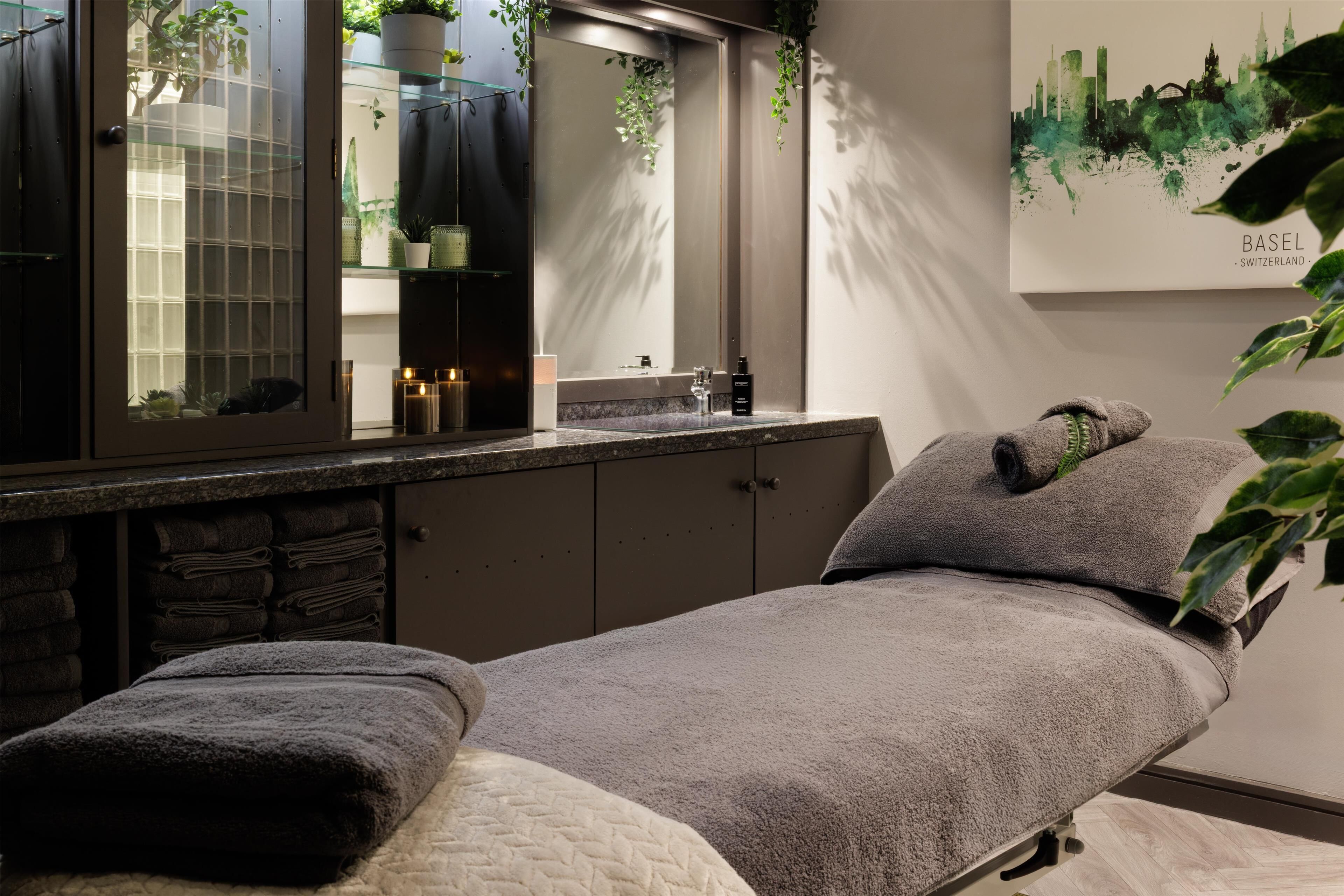 A modern spa room with a bed, a glass-enclosed vanity, and a cityscape artwork.