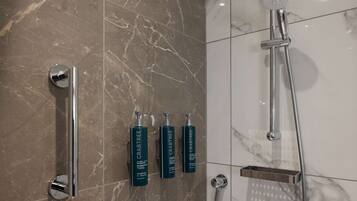 Un bagno con pavimento in marmo, una doccia con soffione a mano e tre flaconi di shampoo Crabtree.