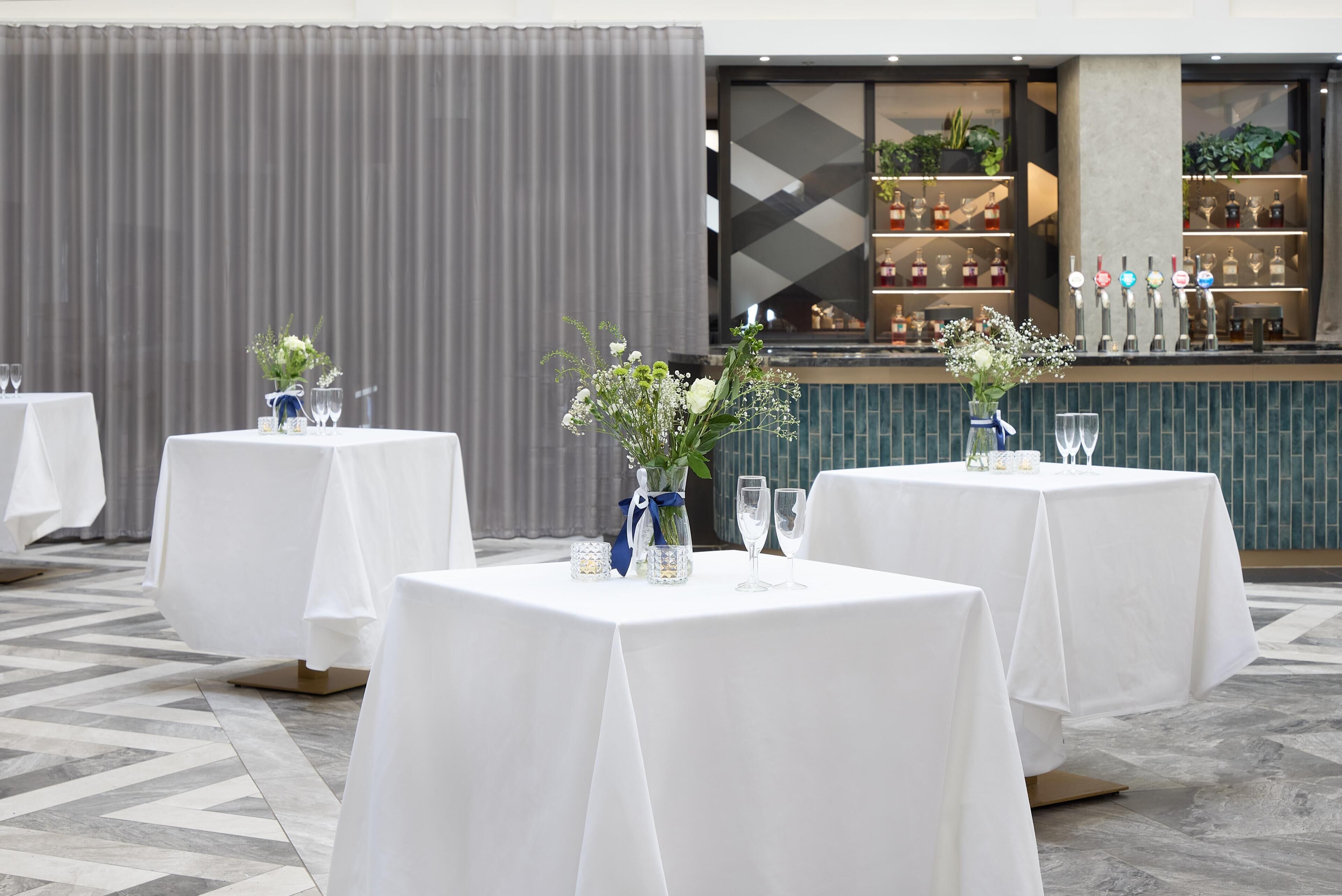 A restaurant with round tables, each with a vase of flowers and wine glasses.