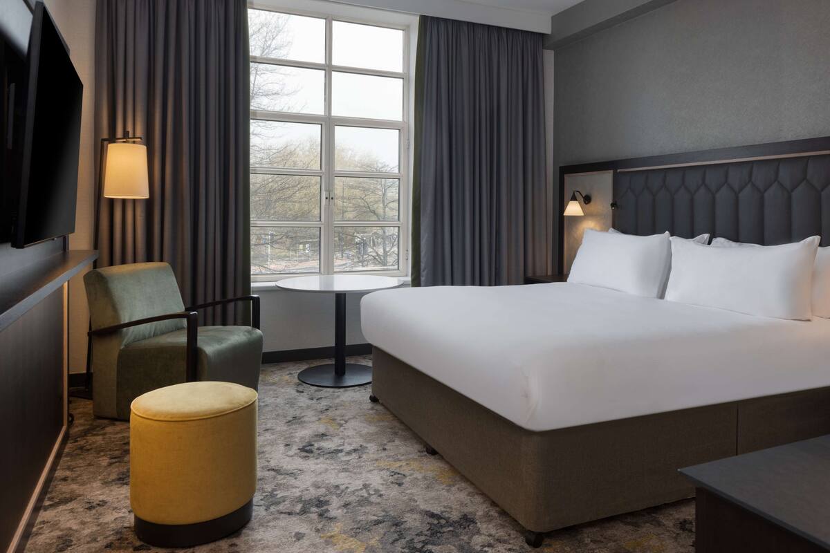 A hotel room with a large bed, a chair, a small table, and a TV.