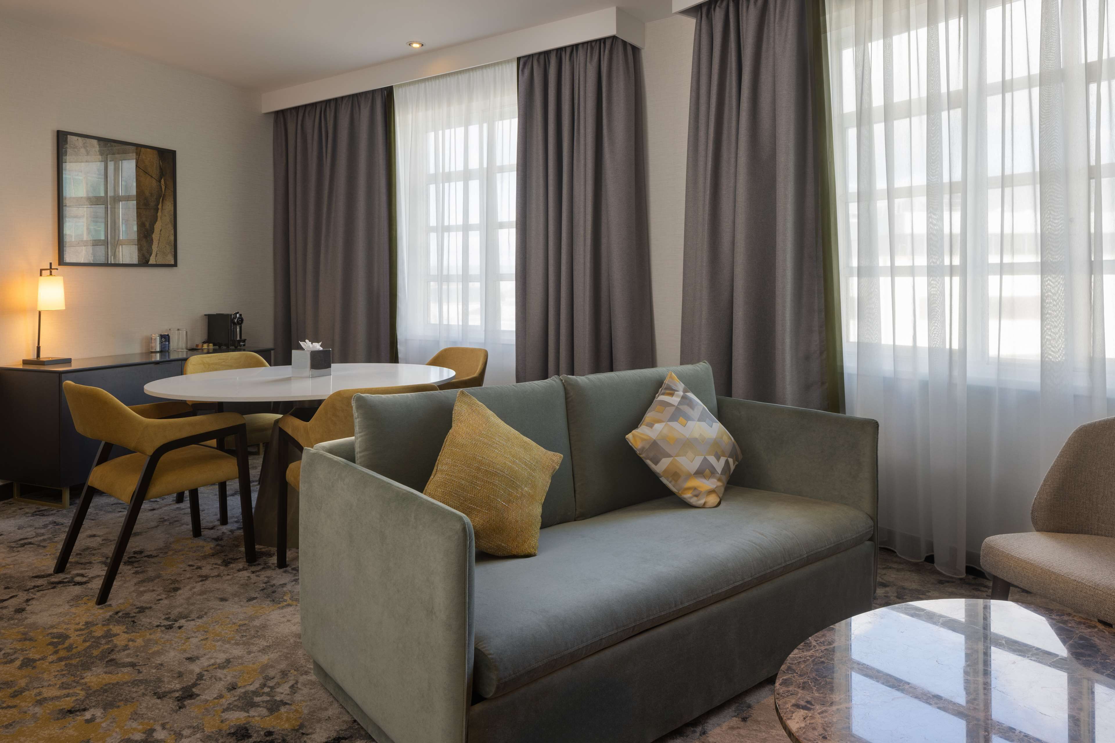 A modern hotel room with a sofa, a round table, and a dining area.