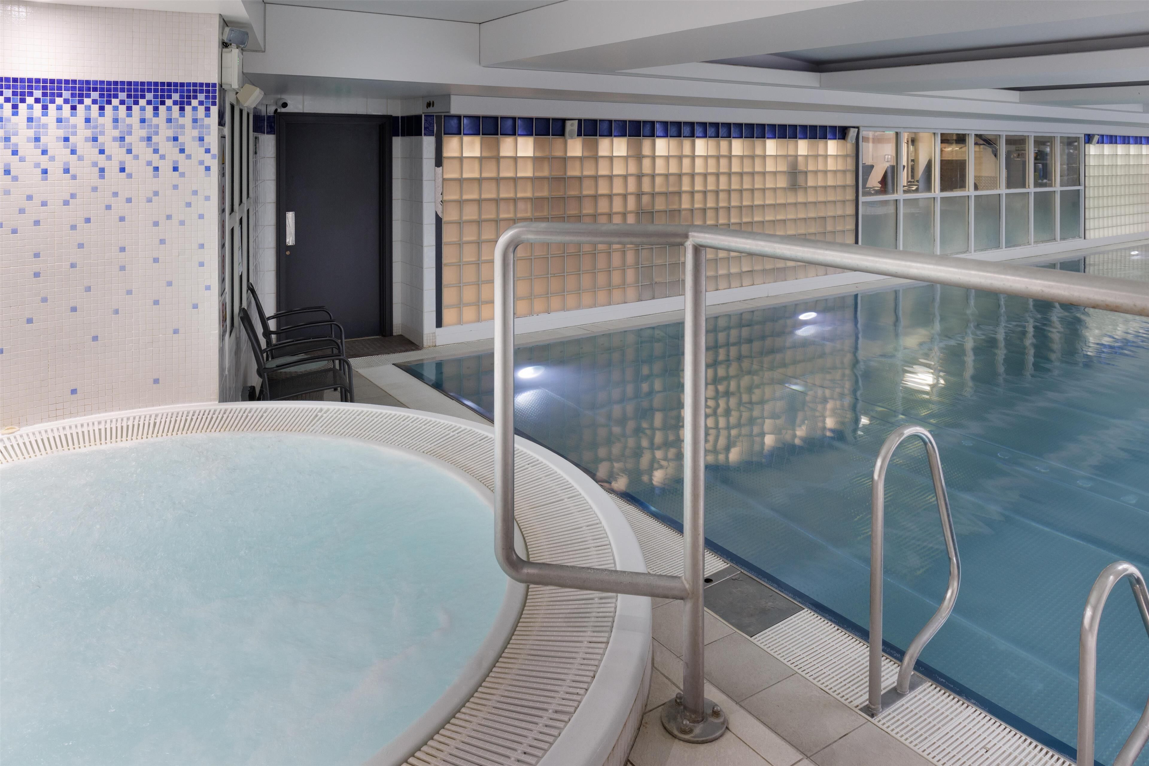 Una piscina interior con superficie de agua cristalina, barandillas metálicas y una pared de azulejos con diseño azul.