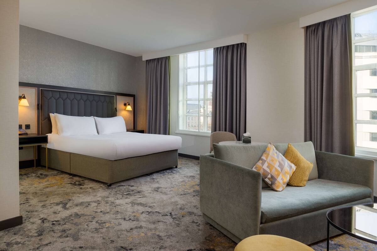 A hotel room with a bed, a sofa, a desk, and a window with curtains.