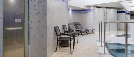 A modern spa area with a glass-enclosed pool, tiled walls, and several lounge chairs.