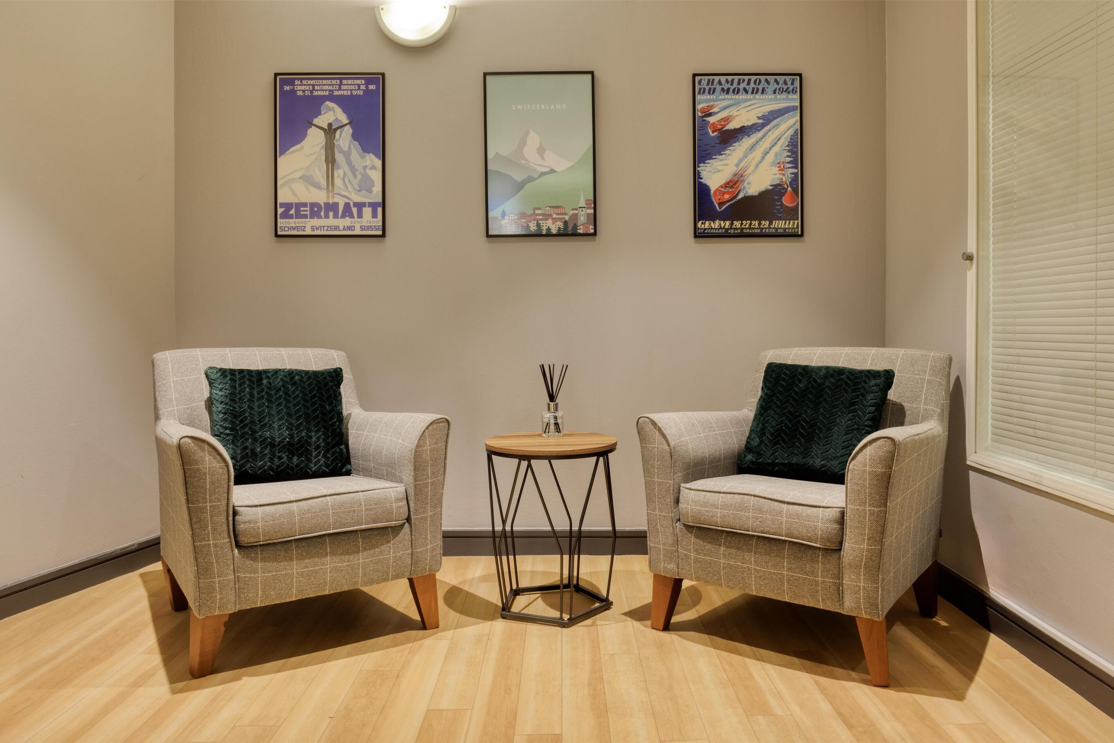A room with two armchairs, a small round table, and three framed posters on the wall.