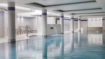 A large indoor swimming pool with clear water, surrounded by white pillars and tiled walls.