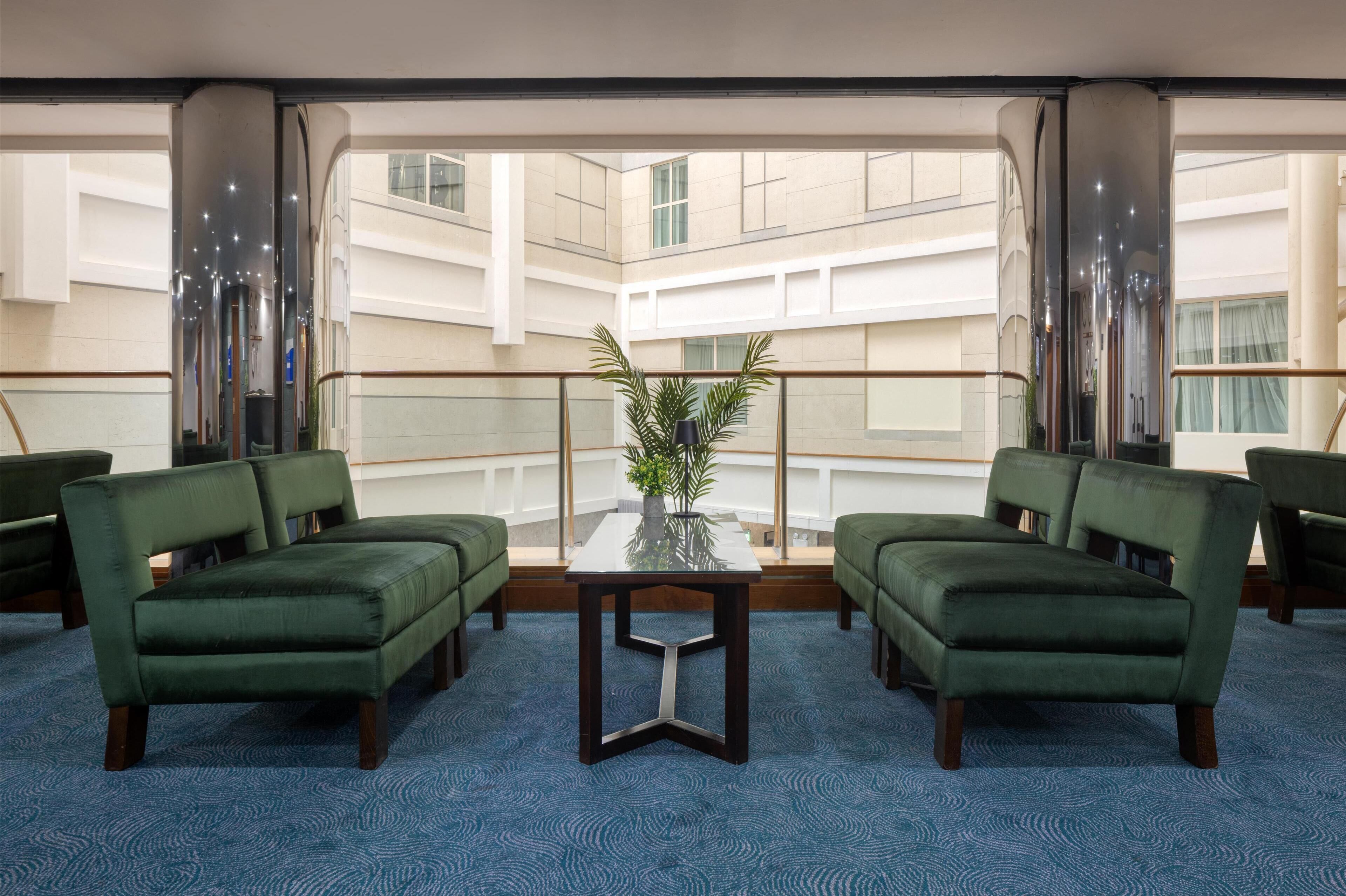 A modern hotel lobby with a glass table, green sofas, and a view of the building's interior.