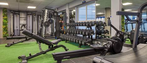 Une salle de sport équipée de matériel de musculation, de tapis de course et recouverte d’une moquette verte.