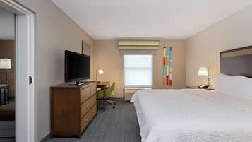 A hotel room with a bed, a TV on a wooden dresser, a desk with a chair, and a window with blinds.