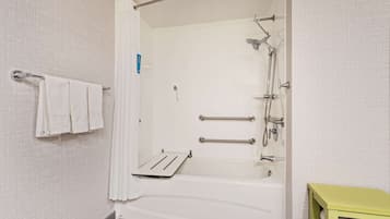 Un baño con bañera, ducha y barras de apoyo. Hay un perchero con toallas y un armario verde.