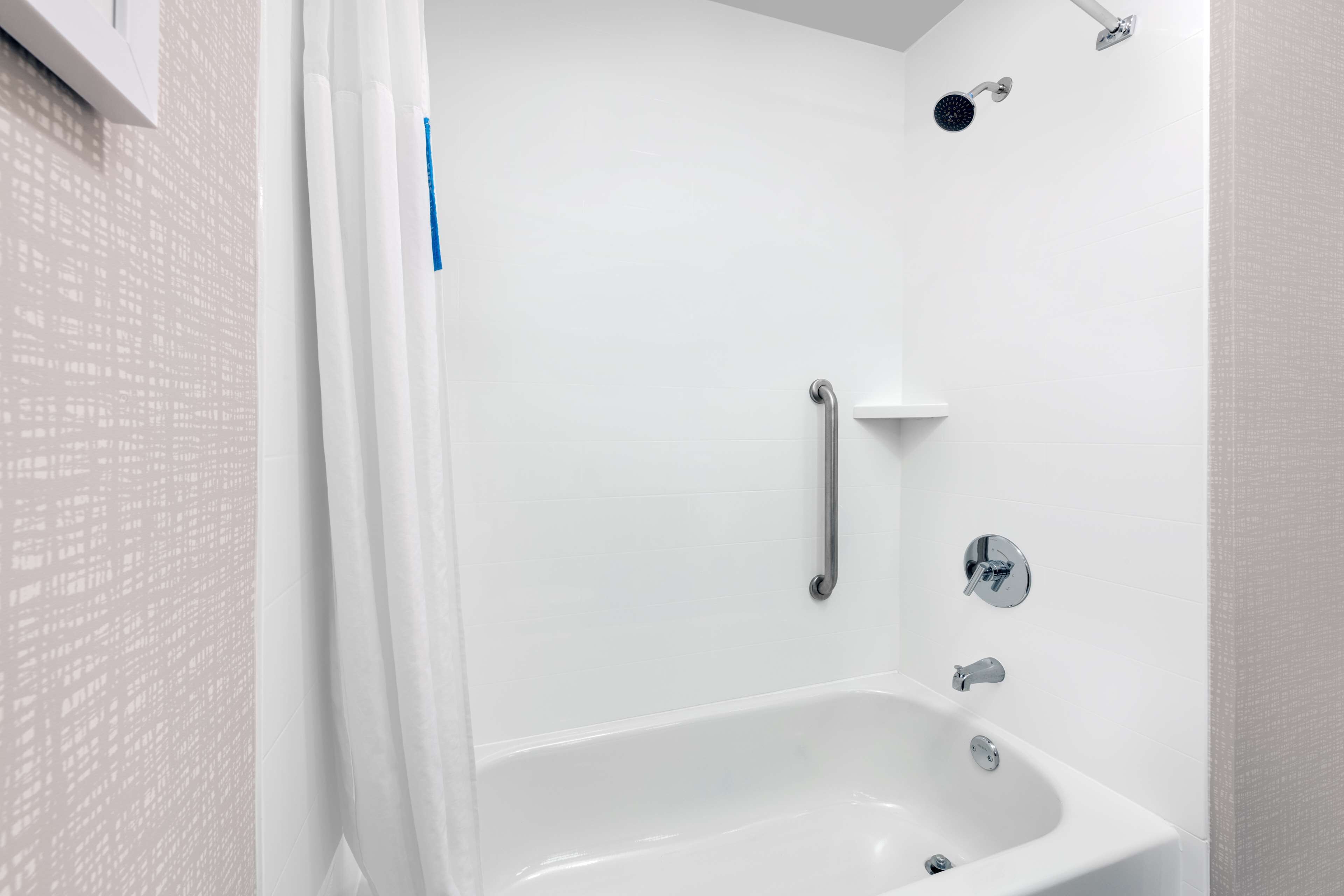 A bathroom with a bathtub, a showerhead, and a handrail.