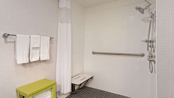 Área de chuveiro com barra de apoio, porta-toalhas com toalhas brancas e um banco verde.