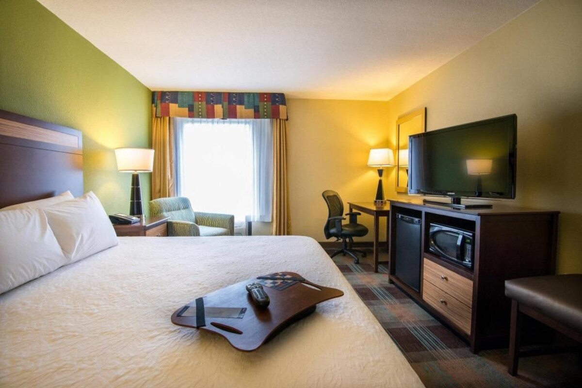 A hotel room with a large bed, a desk with a television, a chair, a desk lamp, and a microwave.