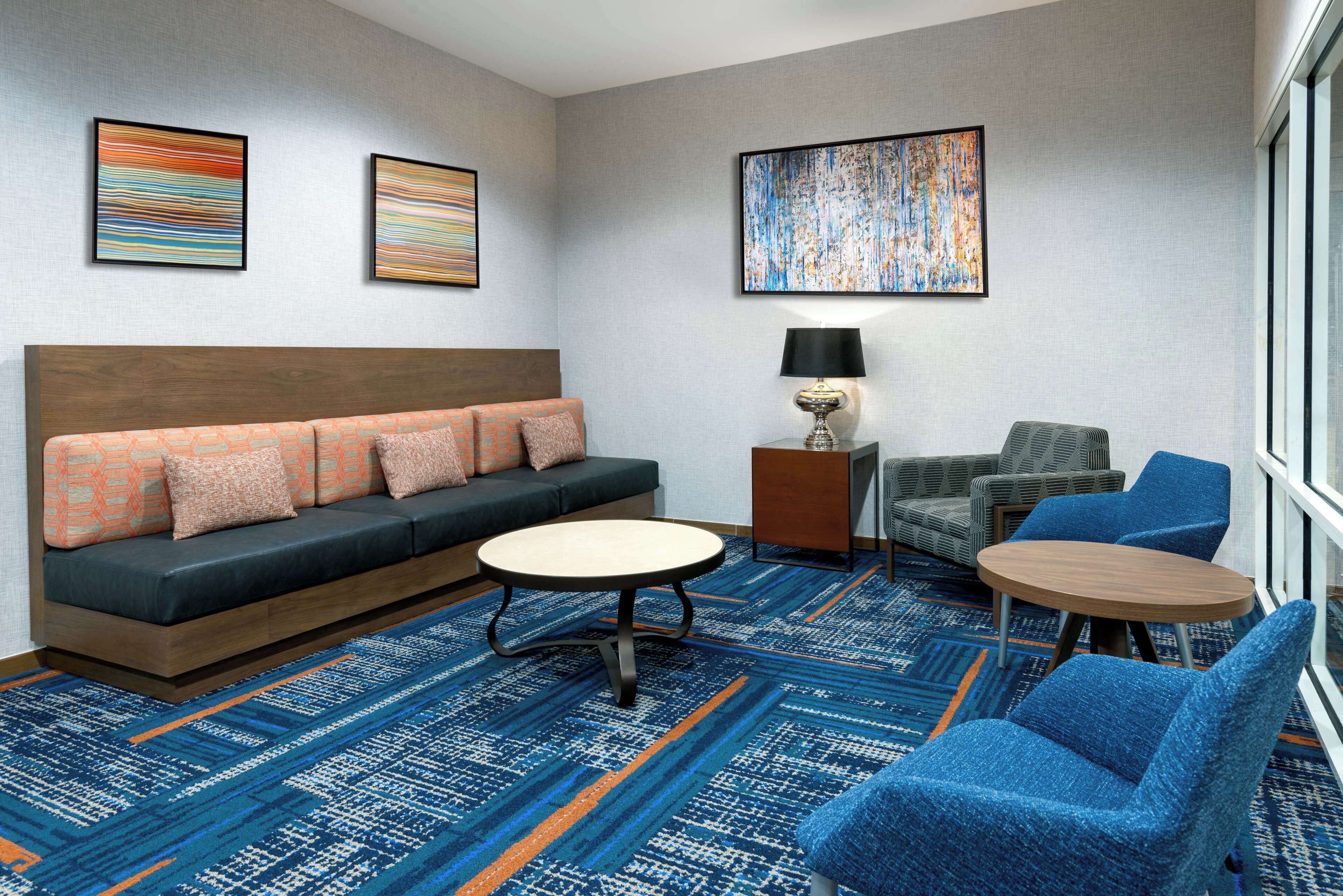 Una habitación de hotel moderna con un sofá, dos sillones, una mesita y una lámpara.