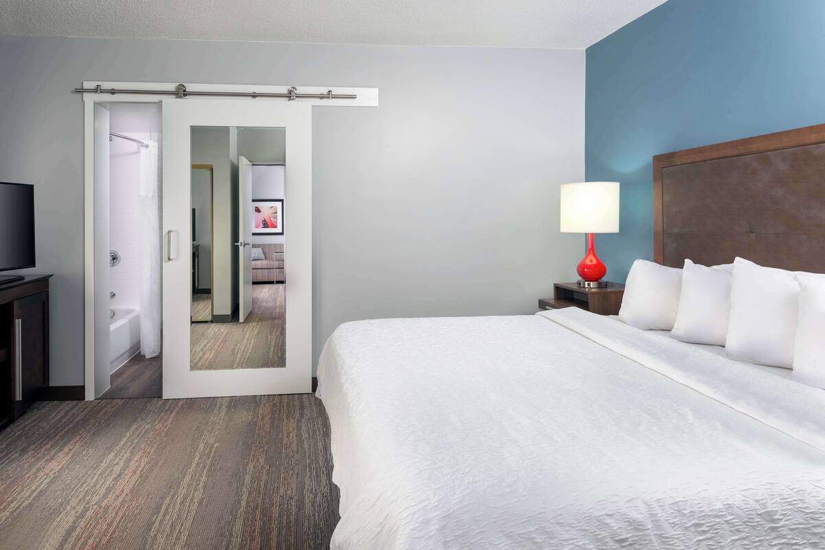 Une chambre d’hôtel avec un lit, une télévision, une lampe rouge et une porte coulissante donnant sur une salle de bain.