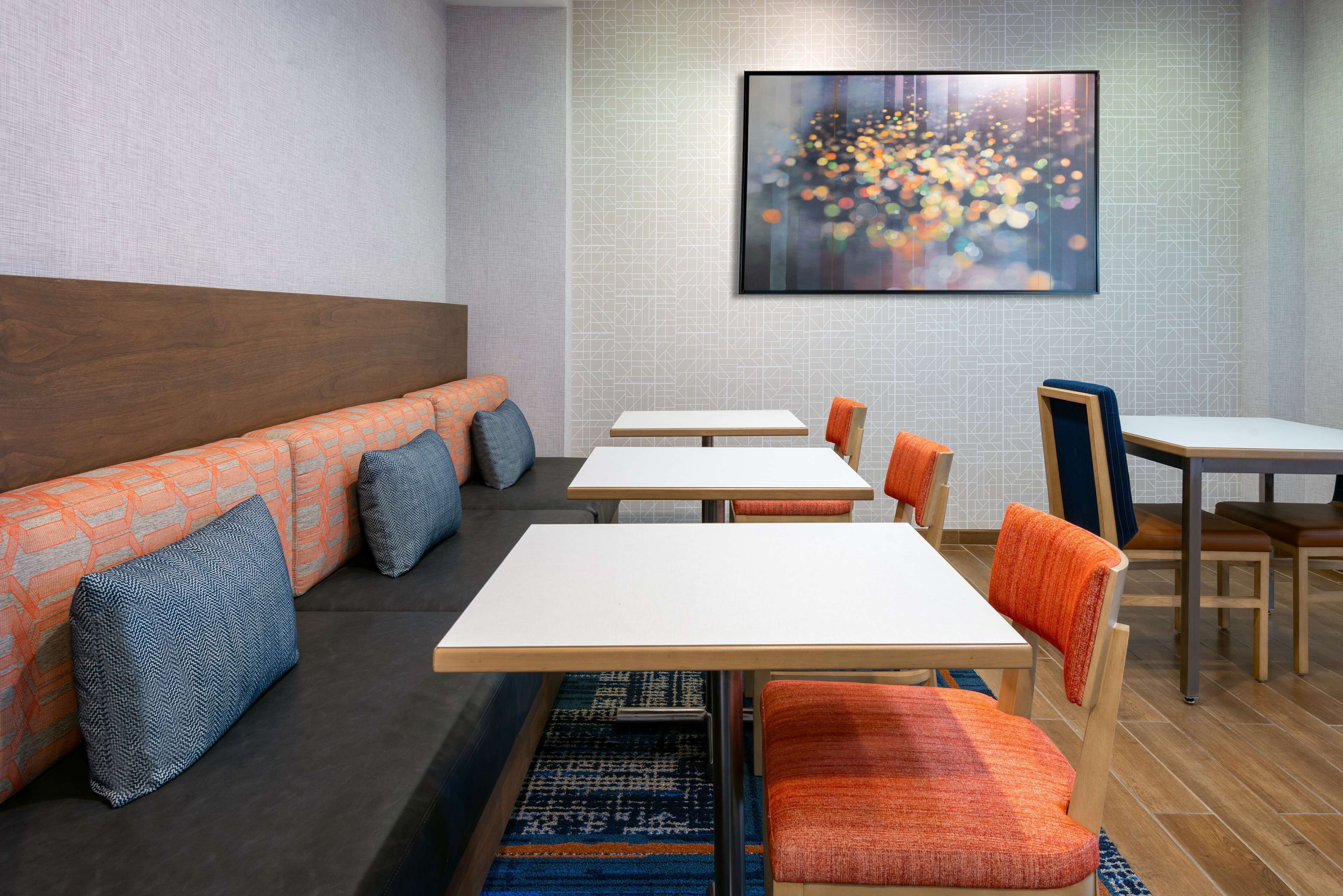 Un espace de restauration moderne avec une longue table et des bancs, un mur décoré de motifs et une œuvre d’art représentant un paysage urbain.