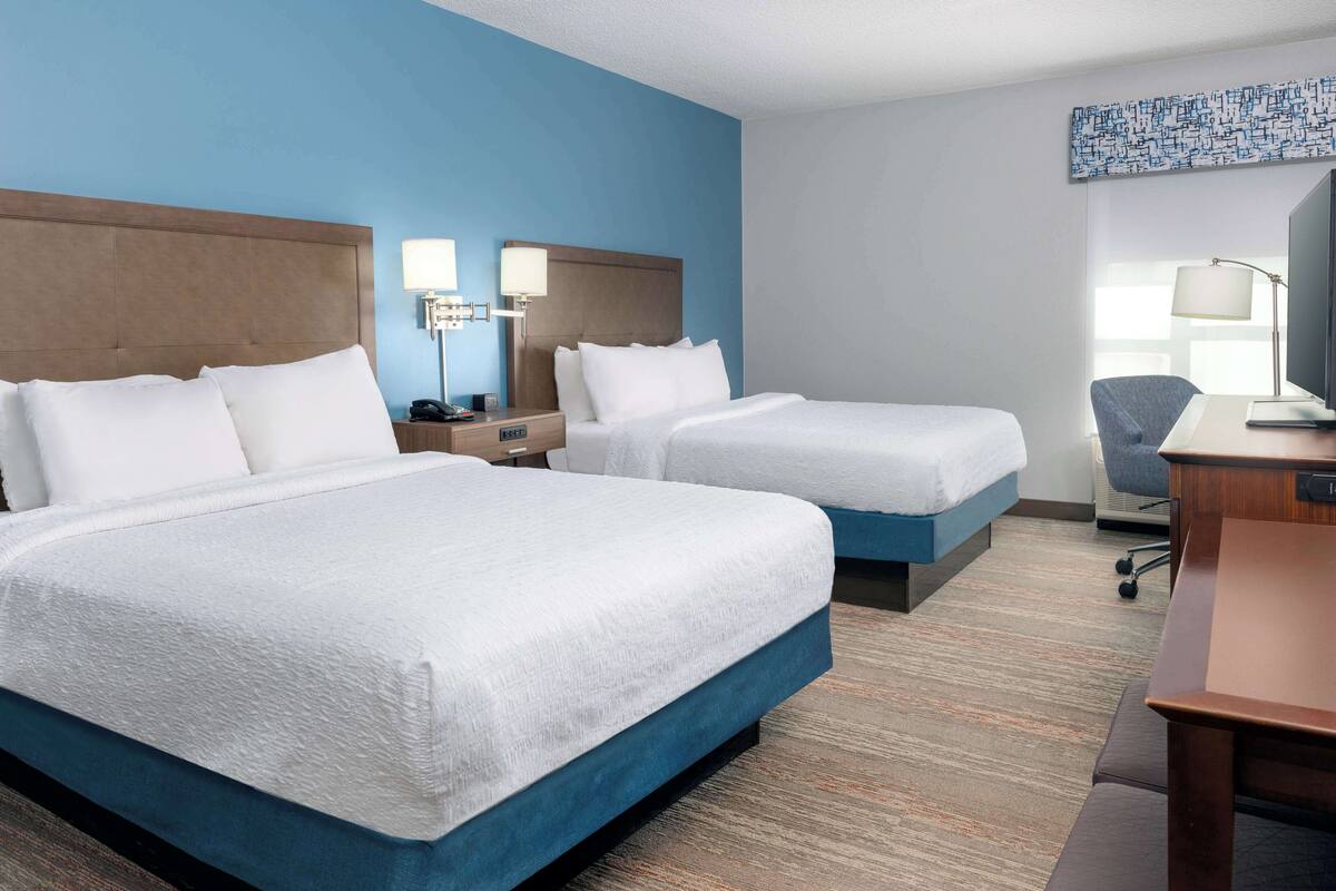 Une chambre d’hôtel avec deux lits, un bureau, une chaise et un téléviseur.