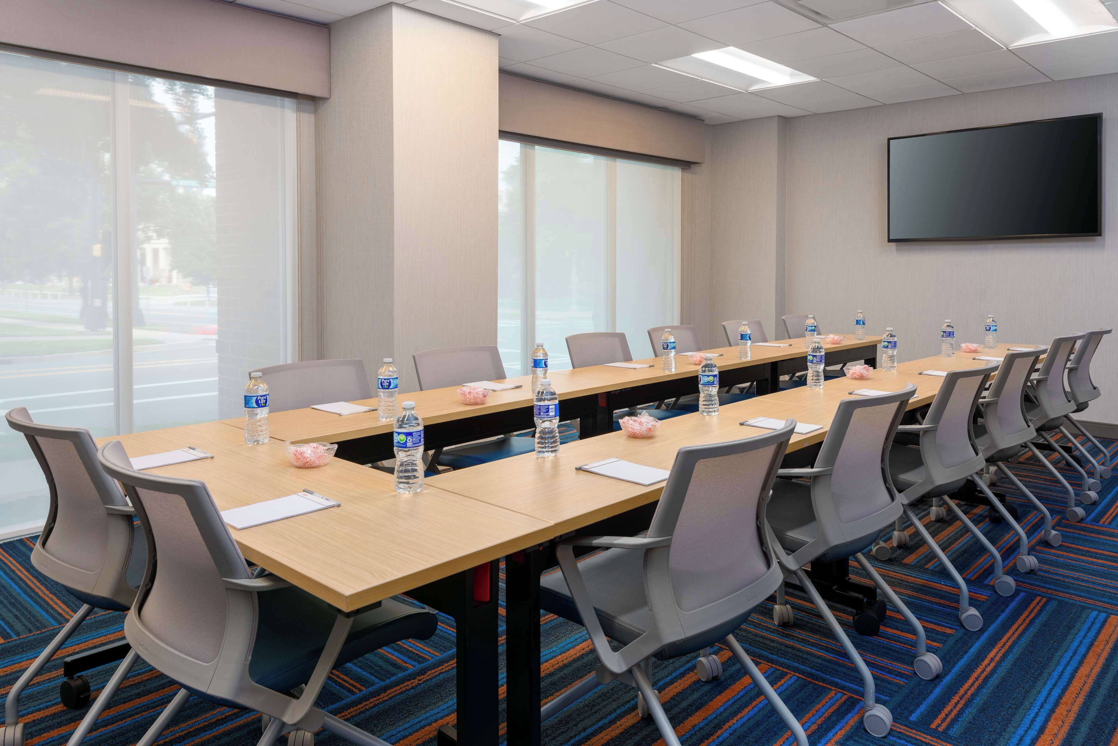 A conference room with a long table, chairs, water bottles, and a flat-screen TV on the wall.