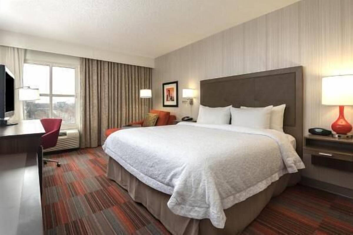 Une chambre d’hôtel avec un grand lit, un bureau, une chaise, une télévision et une fenêtre avec des rideaux.