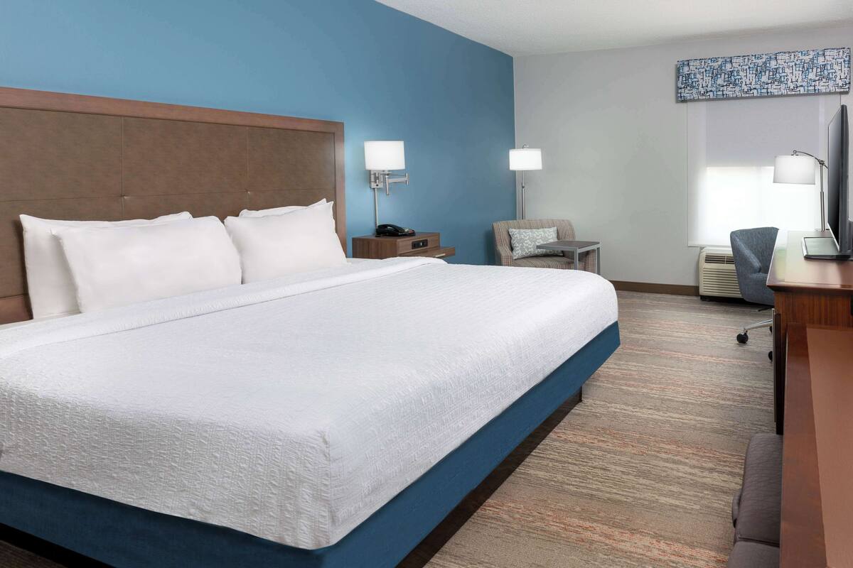 Une chambre d’hôtel avec un grand lit, deux tables de chevet avec des lampes, un bureau avec une chaise et un téléviseur.