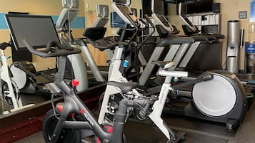 Un gimnasio con bicicletas estáticas, cintas de correr y un espejo grande.