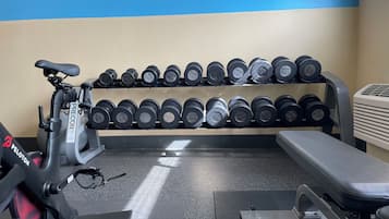Un gimnasio con una bicicleta estática, una banca y un estante con mancuernas.
